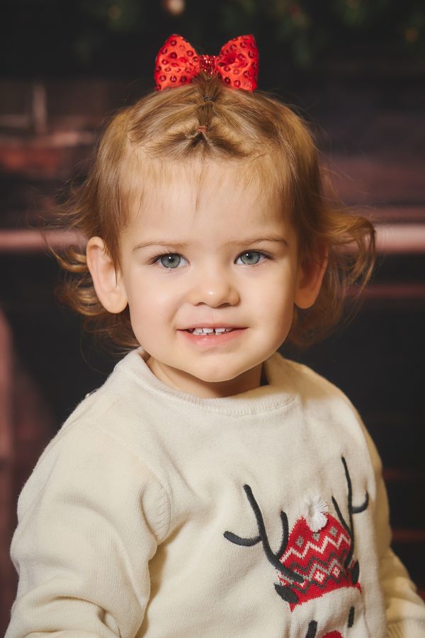Portrait d'une petite fille souriante au nœud rouge à paillettes, décor de Noël chez Aubert