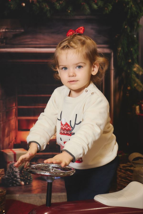 Petite fille penchée sur le volant d'une petite voiture rouge, devant une cheminée de Noël, chez Aubert à Coudekerque-Branche