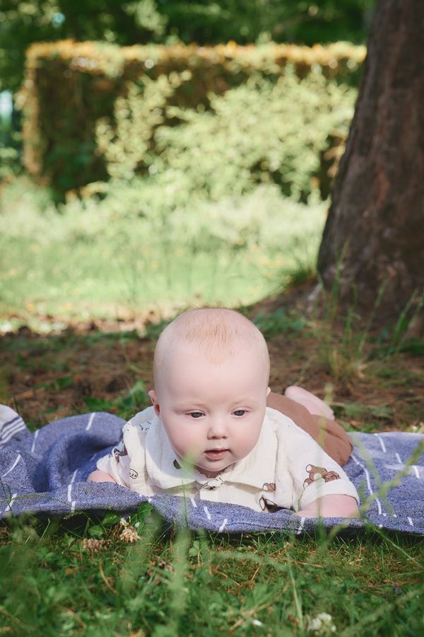 Bébé de 4 mois allongé sur le ventre sur un plaid bleu, menton relevé, aux Jardins du Colysée à Lambersart