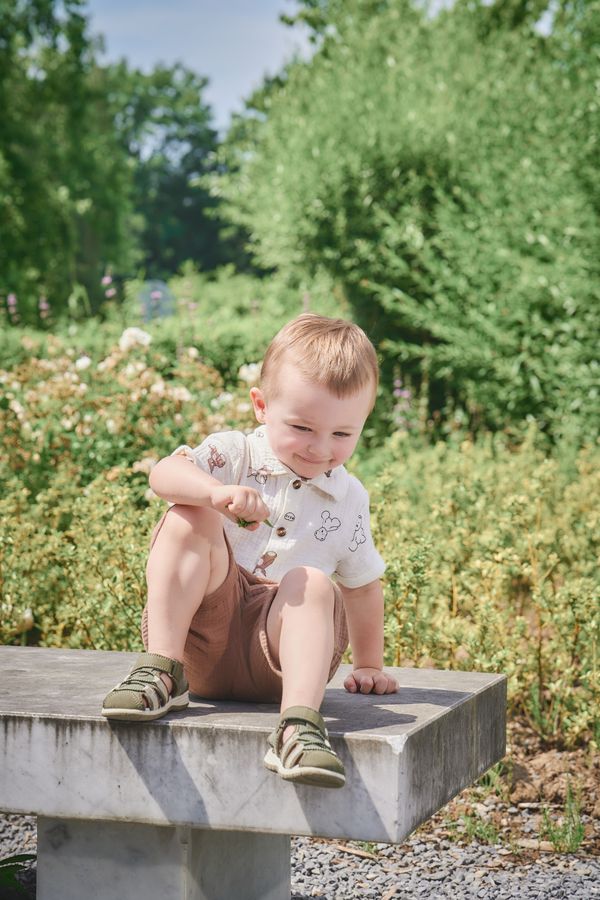 Petit garçon assis sur un banc de pierre, au milieu des massifs des Jardins du Colysée à Lambersart