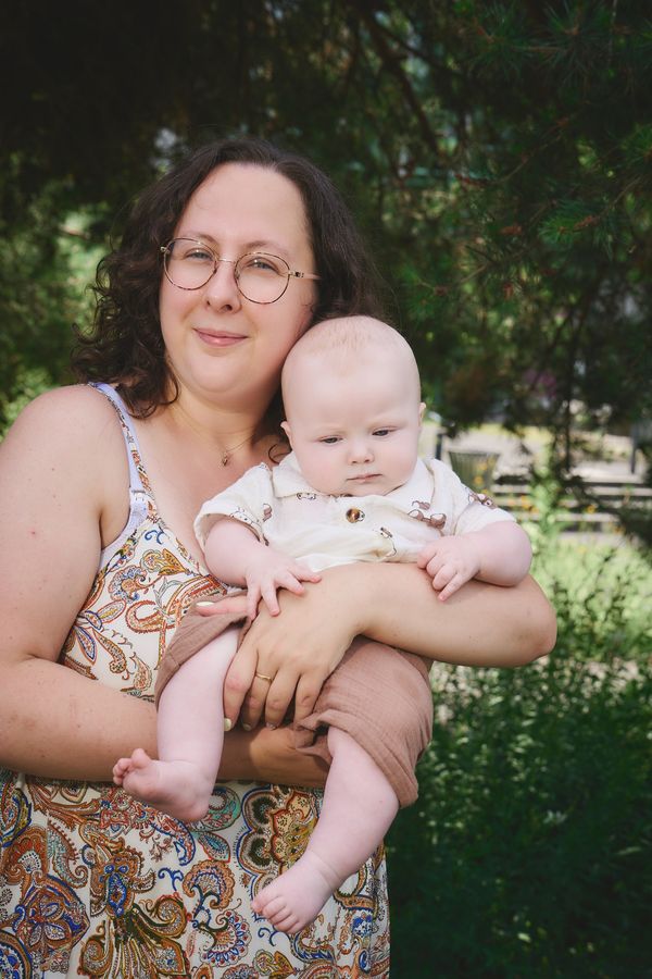 Maman souriante qui tient son bébé de 4 mois dans les bras, dans la verdure des Jardins du Colysée