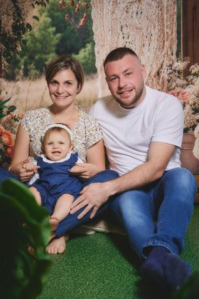 Couple souriant avec leur bébé en salopette, décor de prairie, chez Aubert à Arras