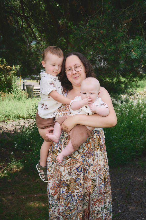 Maman qui porte ses deux jeunes enfants dans un jardin verdoyant, séance photo au parc