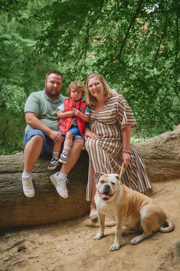 Couple, leur petit garçon et leur bouledogue assis sur un tronc d'arbre en forêt