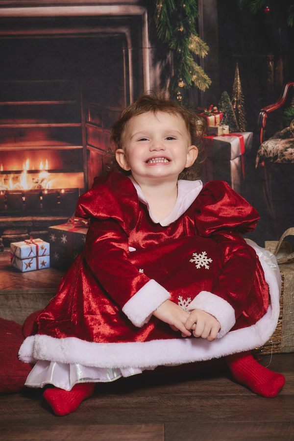 Petite fille en manteau de Mère Noël qui éclate de rire devant la cheminée, chez Aubert à La Sentinelle